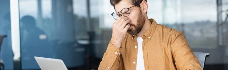 уморен мъж с очила пред лаптоп